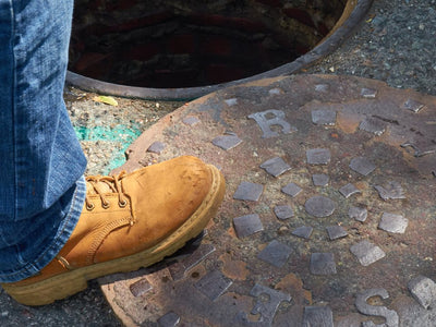 Bota de trabajo junto a una tapa de alcantarilla